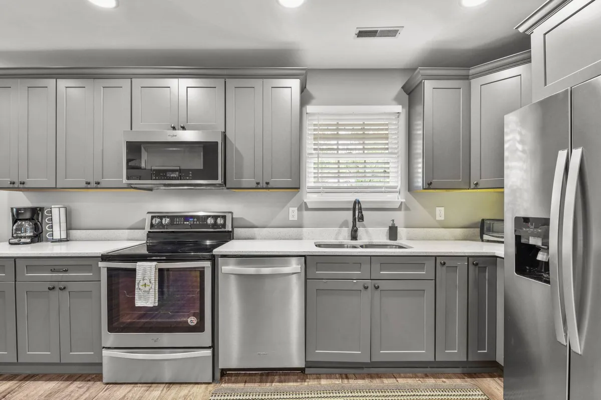 A modern kitchen featuring sleek gray cabinetry, stainless steel appliances, and a well-lit window. The space is organized for easy meal preparation and group cooking, inviting collaboration and culinary creativity.