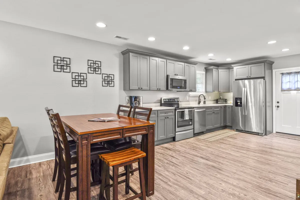 A contemporary kitchen scene featuring a spacious kitchen island, gleaming stainless steel appliances, and an adjacent dining table. The open layout seamlessly connects the kitchen to the living and dining areas, allowing for easy socialization during meal prep. The countertops are well-lit and showcase modern finishes, perfect for culinary creativity.
