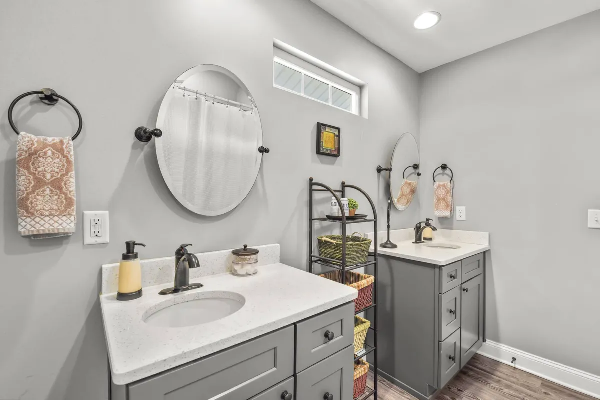 A spacious bathroom featuring double vanity sinks, large mirrors, decorative towels, and a storage rack. The space feels serene and functional—ideal for morning routines or unwinding with evening self-care.