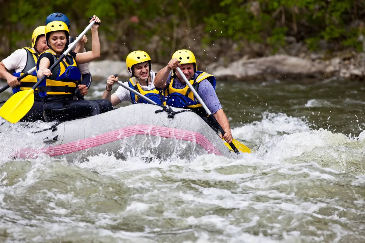 A group of friends navigates a white-water rafting adventure, paddling together as water splashes all around. The participants appear exhilarated, immersed in the excitement and natural beauty of the river.