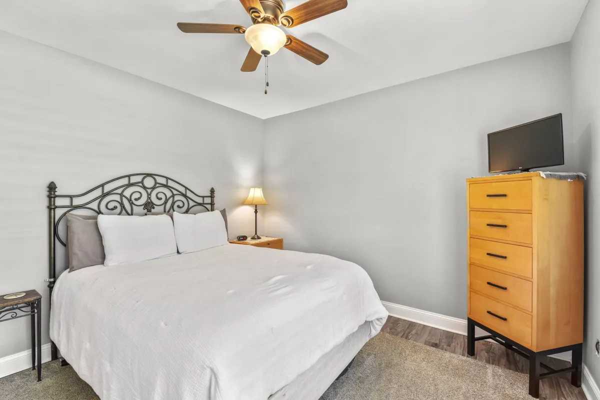 A cozy bedroom with a decorative headboard, a nightstand topped with a lamp, and a dresser with a television. The room exudes a relaxed, welcoming atmosphere, ideal for unwinding after a busy event or for enjoying a restful night’s sleep.