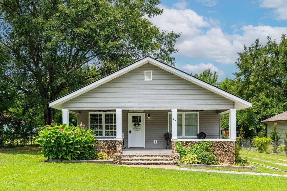 This image features the front porch of the home, framed by landscaped gardens and stone steps, with large windows that hint at the welcoming interior. The porch area is inviting and embodies the spirit of relaxation, perfect for enjoying the scenic mountain views described in the section.