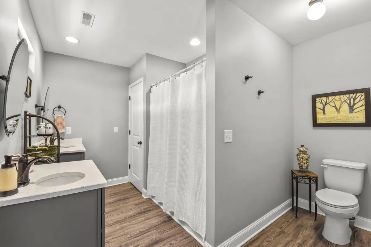 A bright bathroom scene with a vanity, mirror, shower curtain, toilet, and tasteful artwork. Morning sunlight reflects off surfaces for a calm, refreshing ambiance.