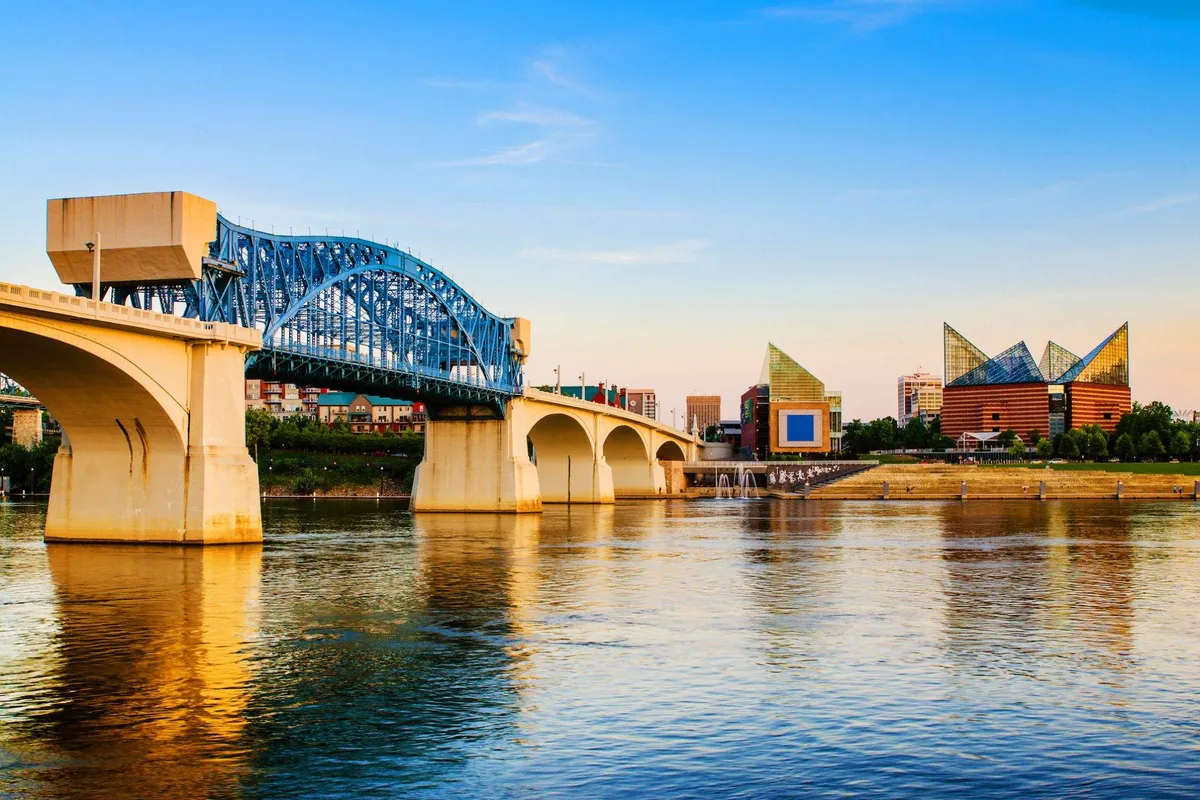 A serene riverside scene featuring a blue bridge, modern buildings, and river reflections. The setting is ideal for picturesque walks, echoing the nearby dog-friendly trails and riverwalks mentioned in the section.