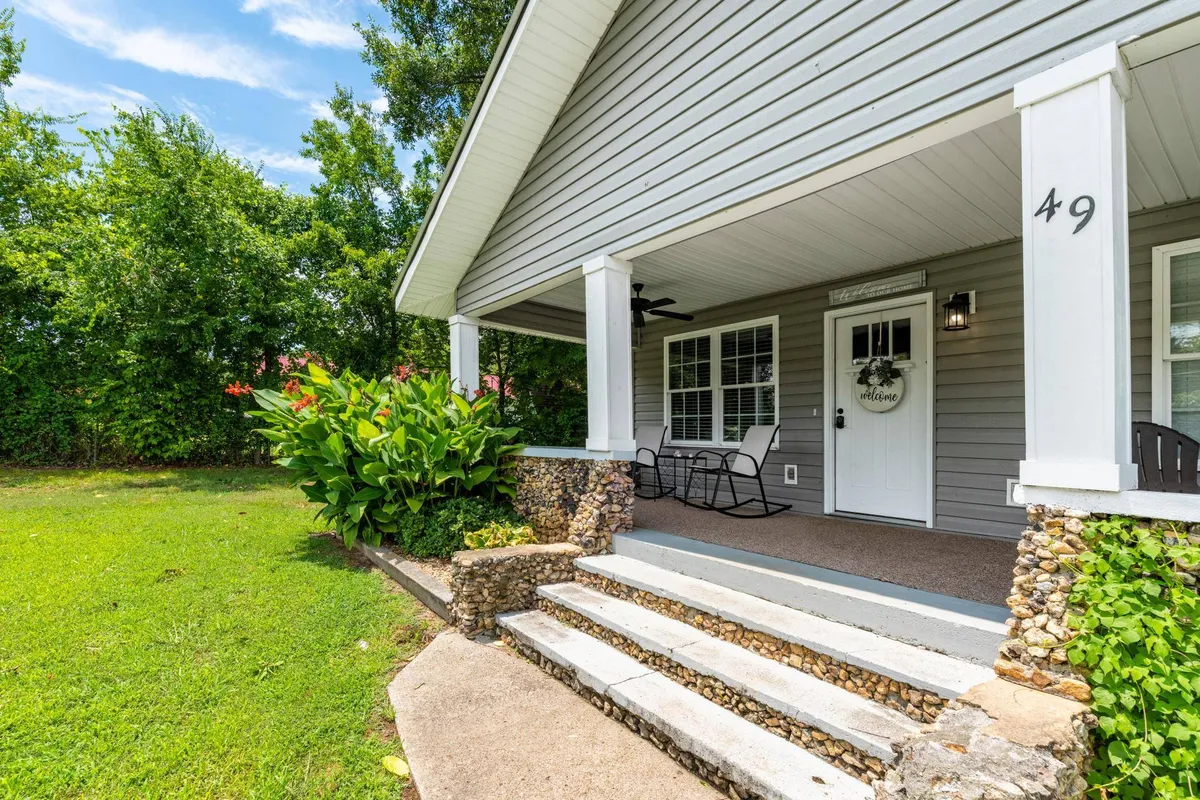 This image displays the inviting front porch of Tennessee Delight, complete with flower beds and steps leading up to the door. The porch is shaded and looks out onto a quiet yard, suggesting a tranquil spot for morning coffee or evening relaxation.