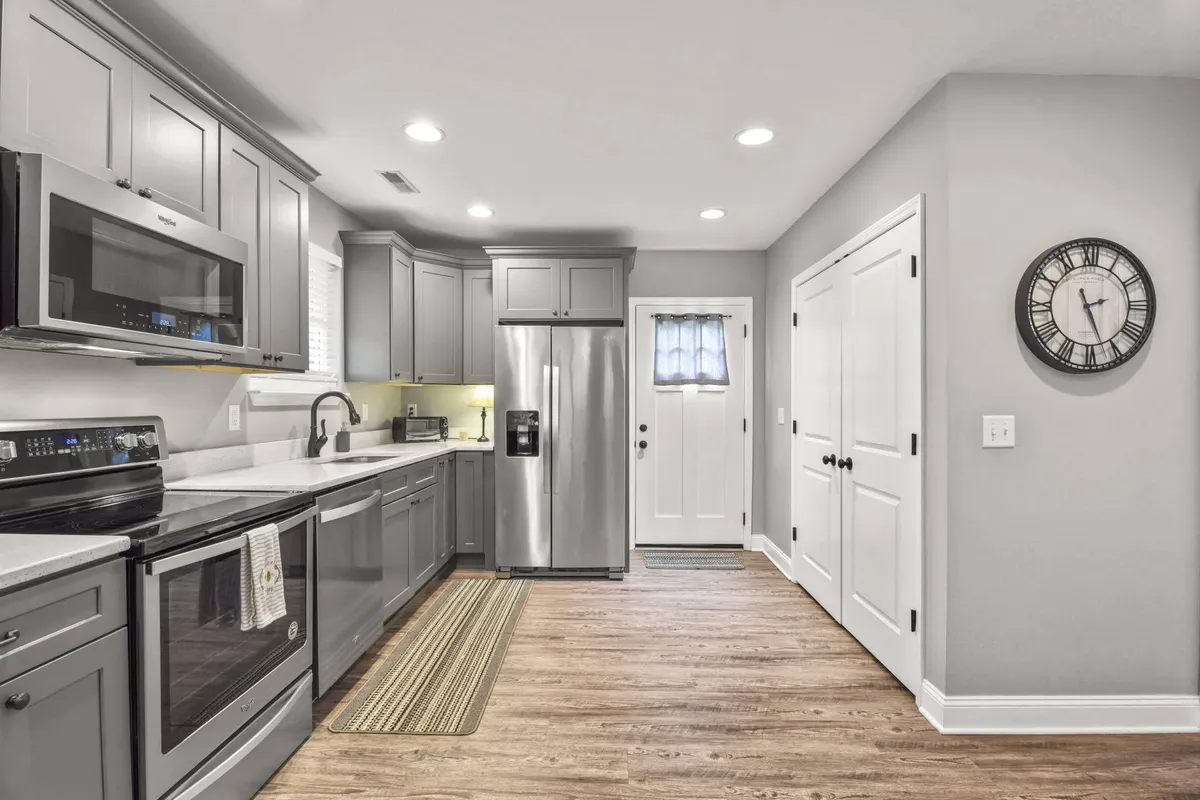 A kitchen with a central island, stainless steel appliances, white cabinetry, and a wall clock. The space is set up for both entertaining and everyday cooking, with plenty of room for guests to gather around. The design is clean and practical, emphasizing both style and functionality.
