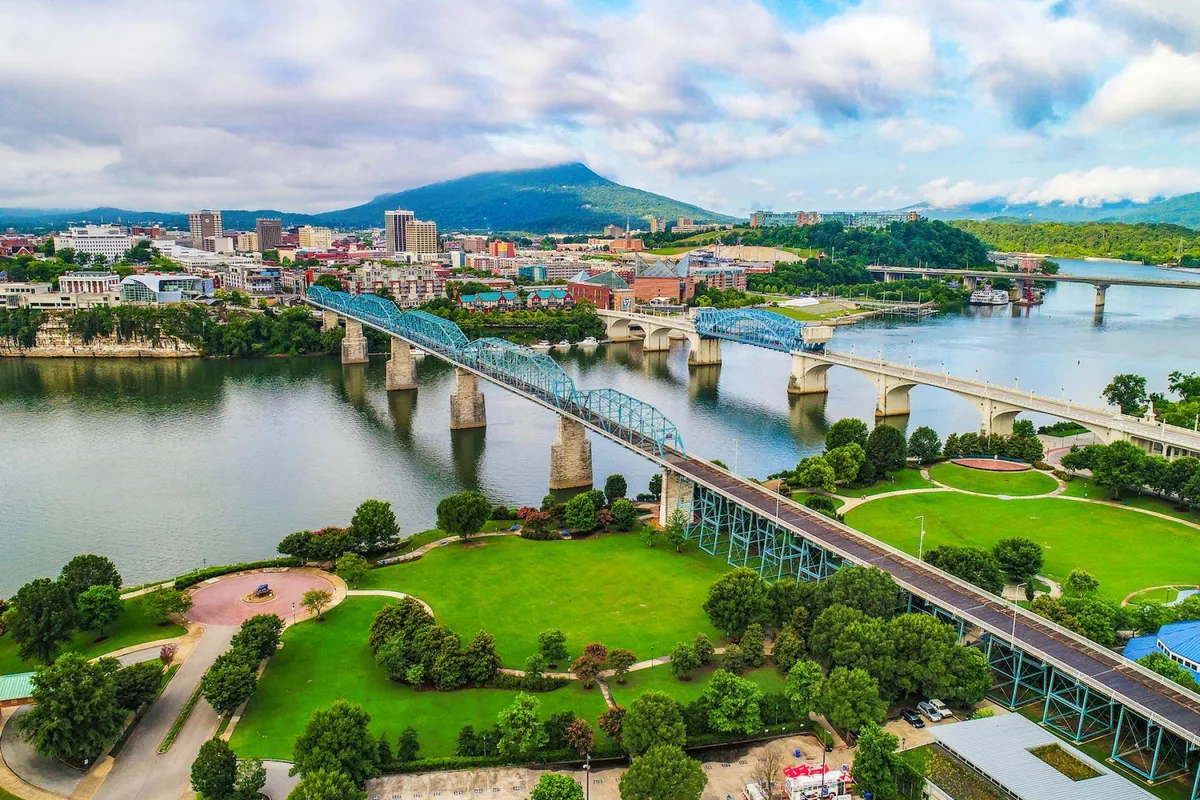 This image offers a dynamic view of the Tennessee River, complete with bridges, Chattanooga’s downtown skyline, a mountain backdrop, and lush green parks. The scene is lively and energetic, suggesting easy access to city attractions and the vibrancy of outdoor activities along the river.