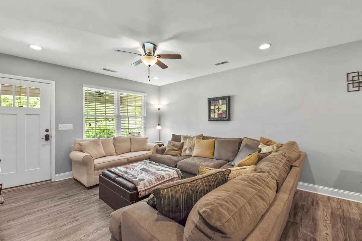 A bright living room centered on a large sectional sofa and a coffee table, with the front door and decorative wall art in view. Natural light pours in, creating an airy yet cozy setting ideal for relaxing, socializing, or enjoying a game night.