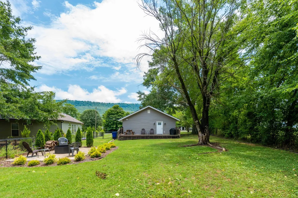 The image showcases a charming single-family house nestled in a tranquil setting, featuring an inviting outdoor seating area under the shade of a mature tree, with stunning mountain views in the background. The scene evokes a sense of peace and relaxation, perfect for unwinding after exploring Chattanooga.